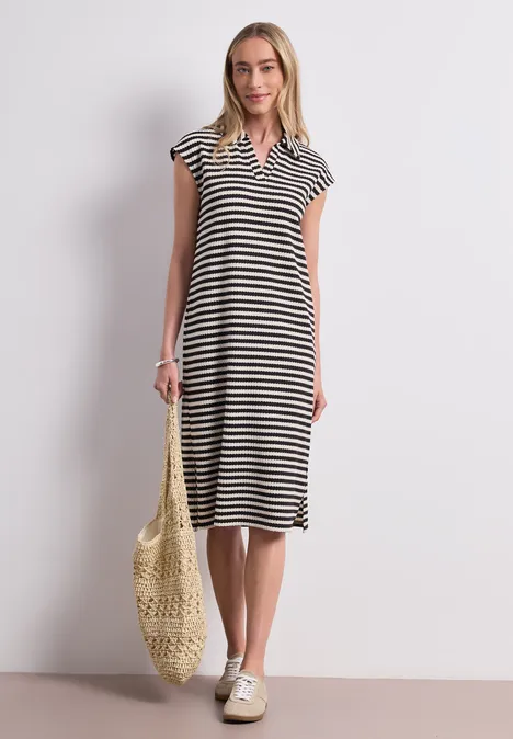 Gebreide midi-jurk met strepen Black Vrouw in zwart-wit gestreepte midi-jurk met V-hals, draagt netzak en sneakers.