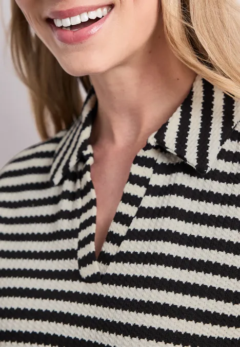Gebreide midi-jurk met strepen Black Vrouw glimlacht, draagt een zwart-wit gestreept poloshirt met kraag.