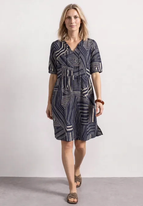 Kniehoge jurk met strikdetail darkest blue Een vrouw draagt een blauw-witte, knielange jurk met V-hals, korte mouwen en sandalen.