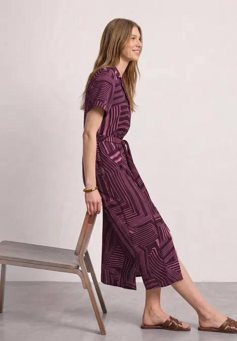 Midi-jurk met bowlingkraag blush berry Vrouw in lila midi-jurk met patroon, staand naast stoel, platte sandalen en armband