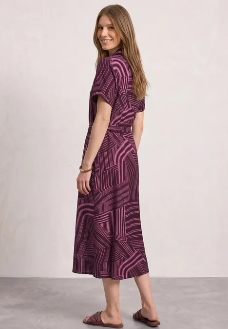 Midi-jurk met bowlingkraag blush berry Zijaanzicht van een vrouw in een paars, gemêleerde midijurk en platte sandalen tegen een neutrale achtergrond.