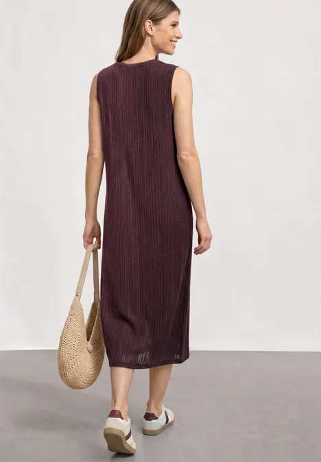 Midijurk van kant met ronde hals rustic rouge Vrouw van achter gezien in mouwloze, geribde midi-bordeauxrode jurk, strooien tas en witte plateausandalen.