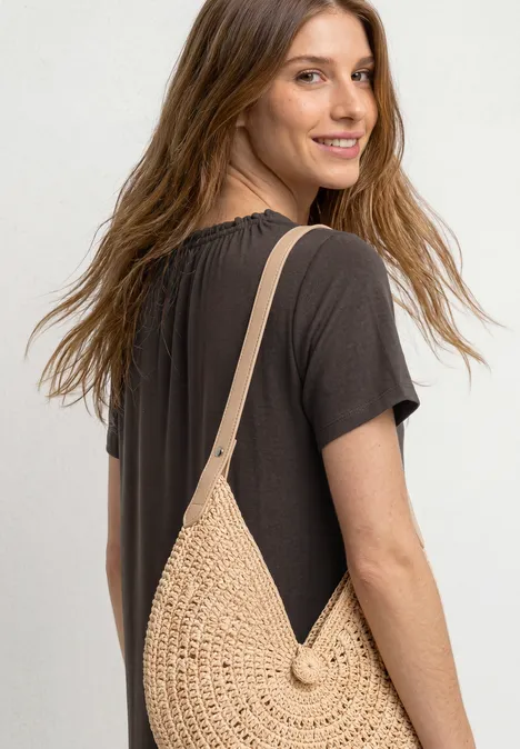 Knielange jersey jurk met ronde hals black coffee Vrouw van achteren in zwarte jurk met ronde, beige stro schoudertas.