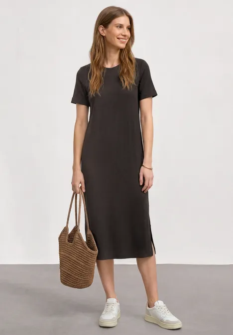 Midijurk met ribbelpatroon en ronde hals black coffee Vrouw in een zwart midi-jurk met korte mouwen, witte sneakers en een rieten tas.