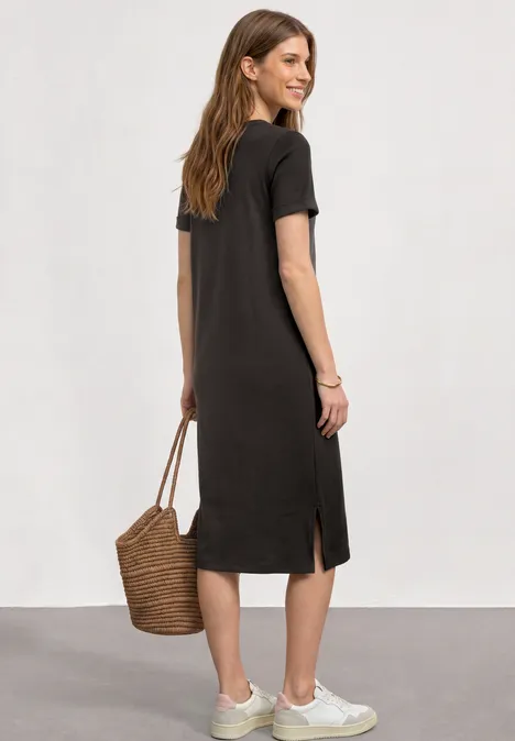 Midijurk met ribbelpatroon en ronde hals black coffee Vrouw van achteren in zwarte midi T-shirtjurk met witte sneakers en rieten tas