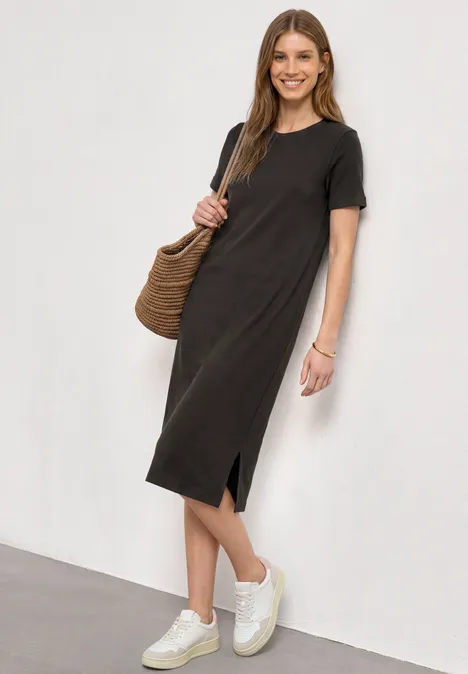 Midijurk met ribbelpatroon en ronde hals black coffee Vrouw in eenvoudige zwarte midi-jurk met korte mouwen, split aan de zijkant, witte sneakers en rieten tas.