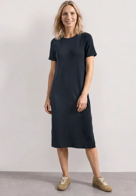 Midijurk met ribbelpatroon en ronde hals darkest blue Een vrouw draagt een simpel donkerblauw midi-T-shirtjurk met lichte sneakers.
