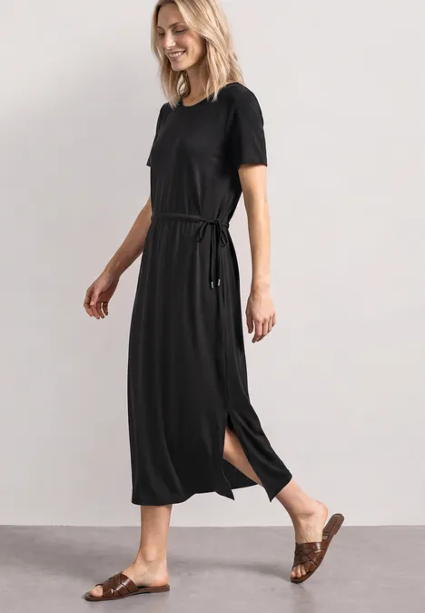Midijurk van jersey met ronde hals Black Een vrouw in een zwarte midi-jurk met korte mouwen, riem en zijsplit, gecombineerd met bruine sandalen.
