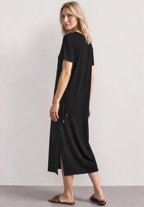 Midijurk van jersey met ronde hals Black Vrouw draagt zwarte midijurk met korte mouwen en zijsplitten, gecombineerd met slippers.