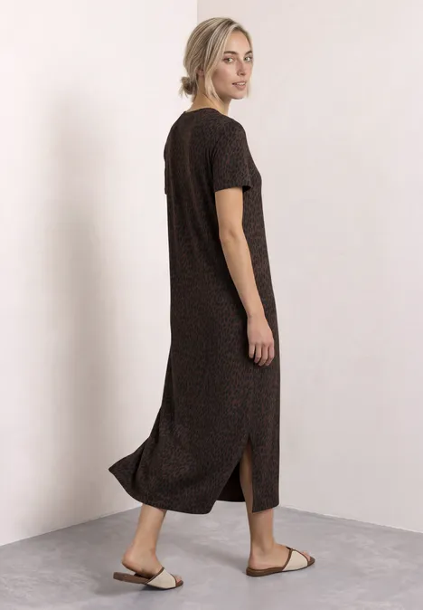 Midi-jurk met grafisch patroon molten earth Vrouw in donkerbruine midi-jurk met korte mouwen en zijsplit, gecombineerd met sandalen, lichte achtergrond.
