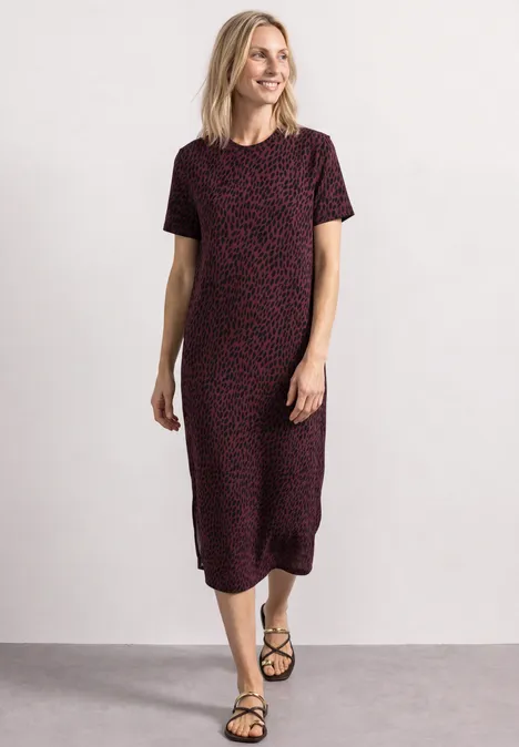Midi-jurk met grafisch patroon rustic rouge Een lachende vrouw draagt een kort roodzwart dessin jurk met zwarte sandalen voor een witte achtergrond.