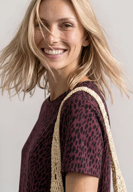 Midi-jurk met grafisch patroon rustic rouge Blonde vrouw lacht, draagt een bordeauxrood topje met luipaardprint en een gevlochten strotas.