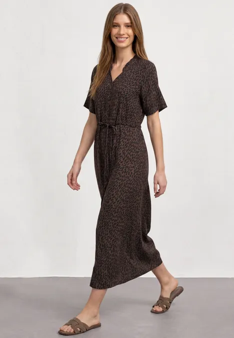 Midi-jurk met V-hals en luipaardprint molten earth Vrouw in een bruine maxi-jurk met ceintuur en sandalen, die glimlachend loopt.