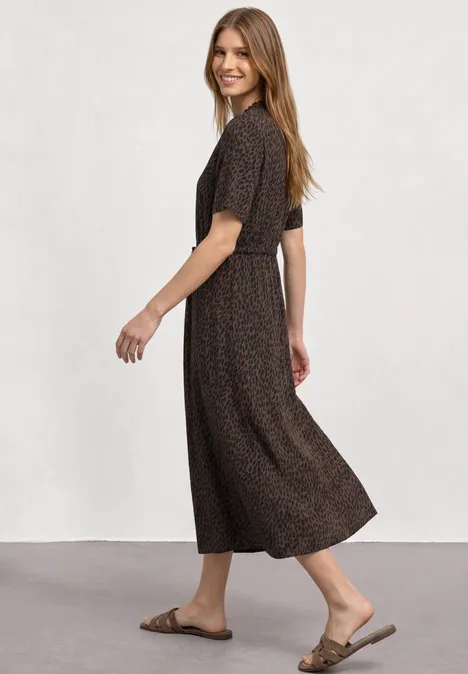 Midi-jurk met V-hals en luipaardprint molten earth Vrouw in een bruin midi-jurk met patroon en sandalen, glimlachend terwijl ze omkijkt.