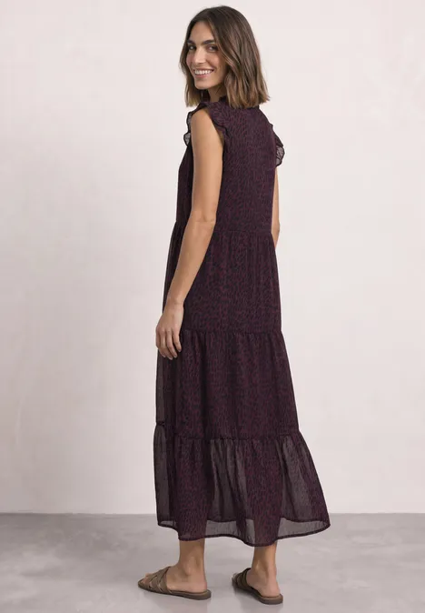 Maxi-chiffonjurk met volants en print rustic rouge Vrouw in een vloeiende, mouwloze midi-jurk met volantjes en subtiel stippenpatroon, gecombineerd met platte sandalen