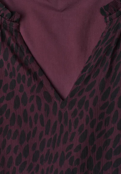 Maxi-chiffonjurk met volants en print rustic rouge Close-up van een bordeauxkleurige V-hals met een zwart druppelpatroon op stof.
