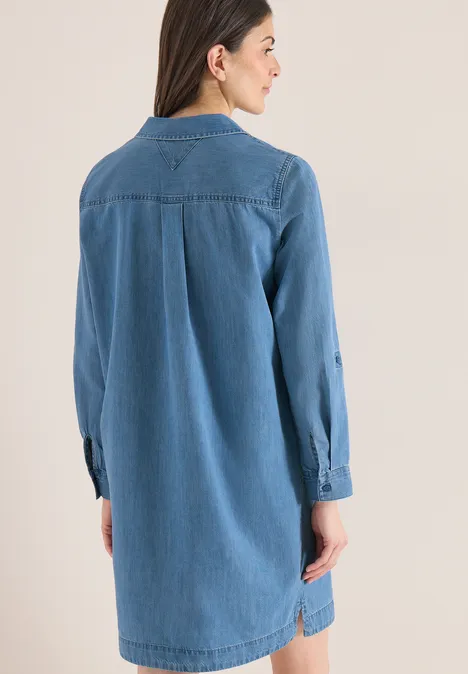 Knielange jurk in denimlook mid blue wash Vrouw van achteren in een losse, knielange spijkershirtjurk met lange mouwen en kraag.