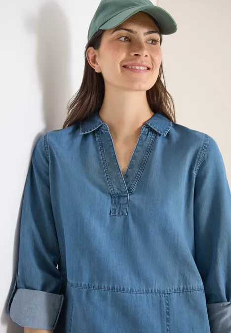 Knielange jurk in denimlook mid blue wash Iemand draagt een lichtblauwe denimblouse met V-hals en opgerolde mouwen en een groene pet.