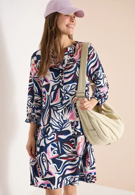 Knielange jurk met grafisch patroon universal blue Vrouw in patroonjurk met roze pet en grote groene schoudertas