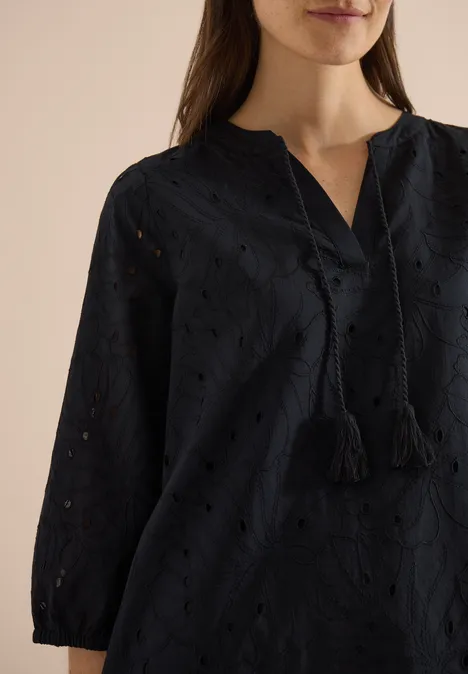 Knielange jurk met 3/4-mouwen en borduursel Black Vrouw draagt zwart geborduurd blouse met oogjes, V-hals en kwastjes aan de koordsluiting.
