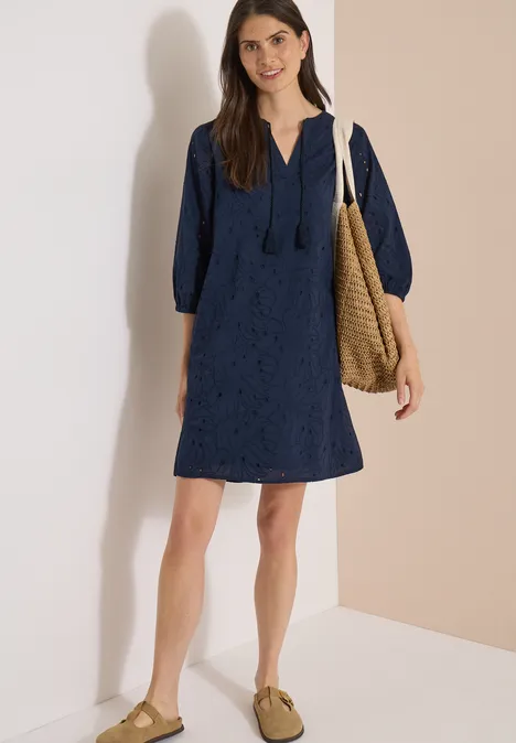 Knielange jurk met 3/4-mouwen en borduursel universal blue Vrouw in korte marineblauwe kanten jurk met capuchon, met een rieten tas en platte schoenen voor lichte achtergrond.