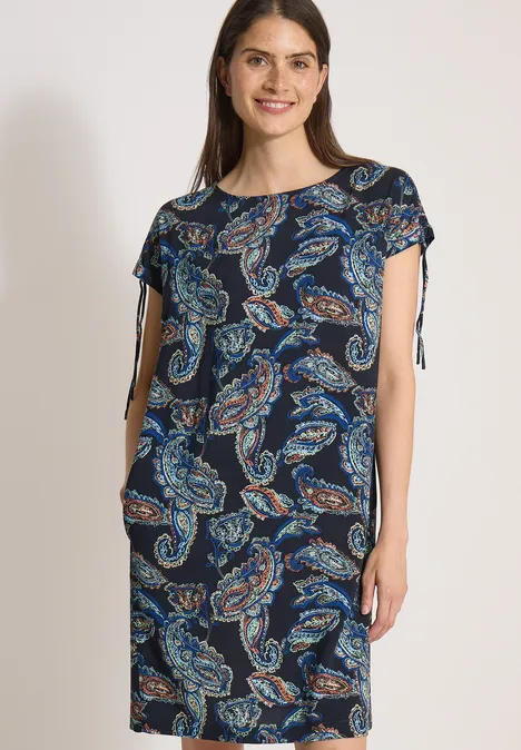 Knie-lange jurk met kapmouwtjes universal blue Vrouw draagt marineblauwe jurk met paisleyprint, korte mouwen en zijstrikjes.