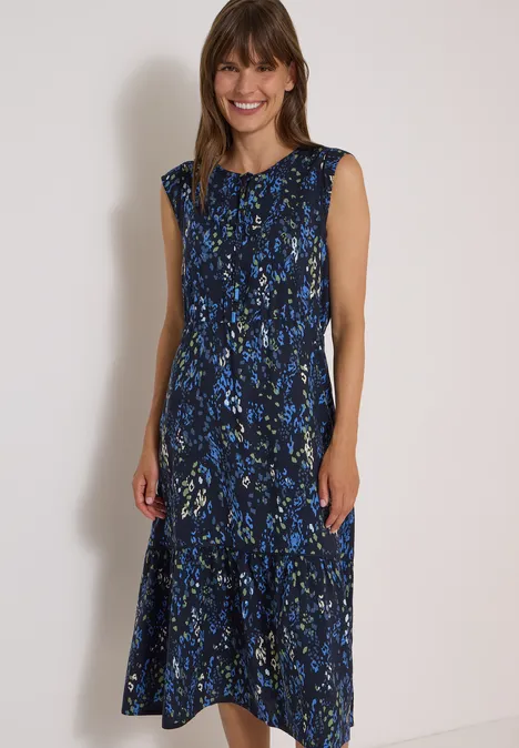Midi-jurk met split in de hals en print urban dark blue Vrouw in mouwloze, lange jurk met blauw bloemenmotief tegen een lichte achtergrond.