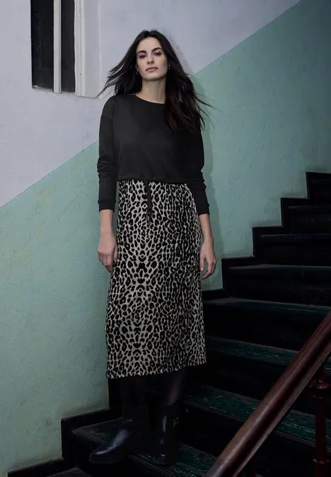 Midi-jurk met leirok Black Vrouw in zwart shirt en luipaardrok met laarzen, staand op trap voor een groen-witte muur.