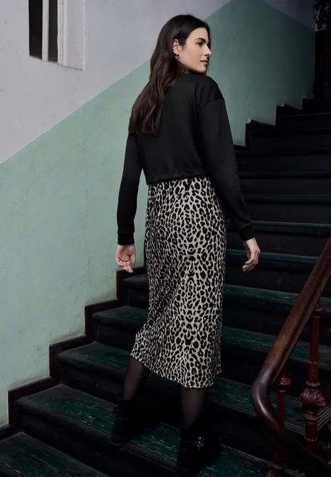 Midi-jurk met leirok Black Persoon in zwarte blouse en luipaardrok loopt een donker trappenhuis op.