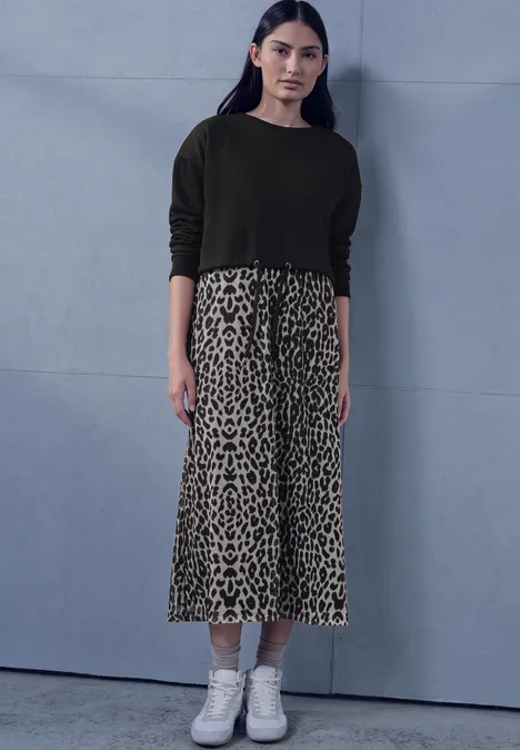 Midi-jurk met leirok Black Model in zwarte trui, midirok met luipaardprint en witte sneakers voor grijze achtergrond