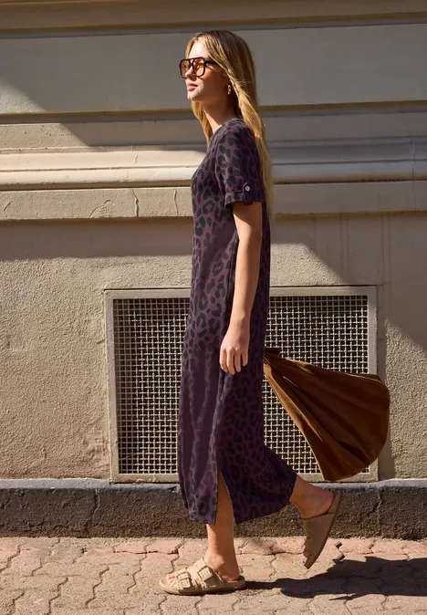 Midijurk met ronde hals en luipaardprint very berry Vrouw in een paars, gebloemd jurkje loopt langs een gevel, met sandalen en een bruine tas.