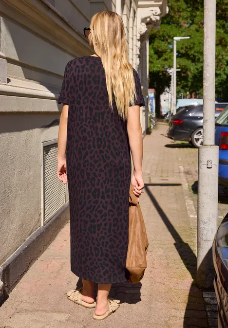 Midijurk met ronde hals en luipaardprint very berry Een vrouw in een lange zwarte jurk met dierenprint loopt over een zonnig trottoir.
