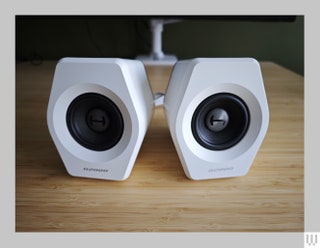 White hexagonal shaped speakers with black centers sitting on wooden surface