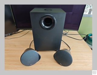 Black rectangular speaker behind two smaller circular speakers all sitting on a wooden surface