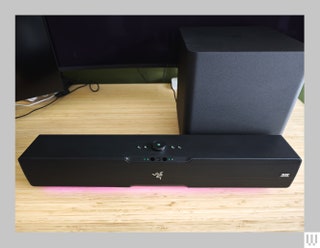 Long black rectangular speaker with small buttons on top sitting on wooden surface