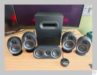 Black square speaker behind 4 cylindrical shaped speakers and a small oval shaped speaker