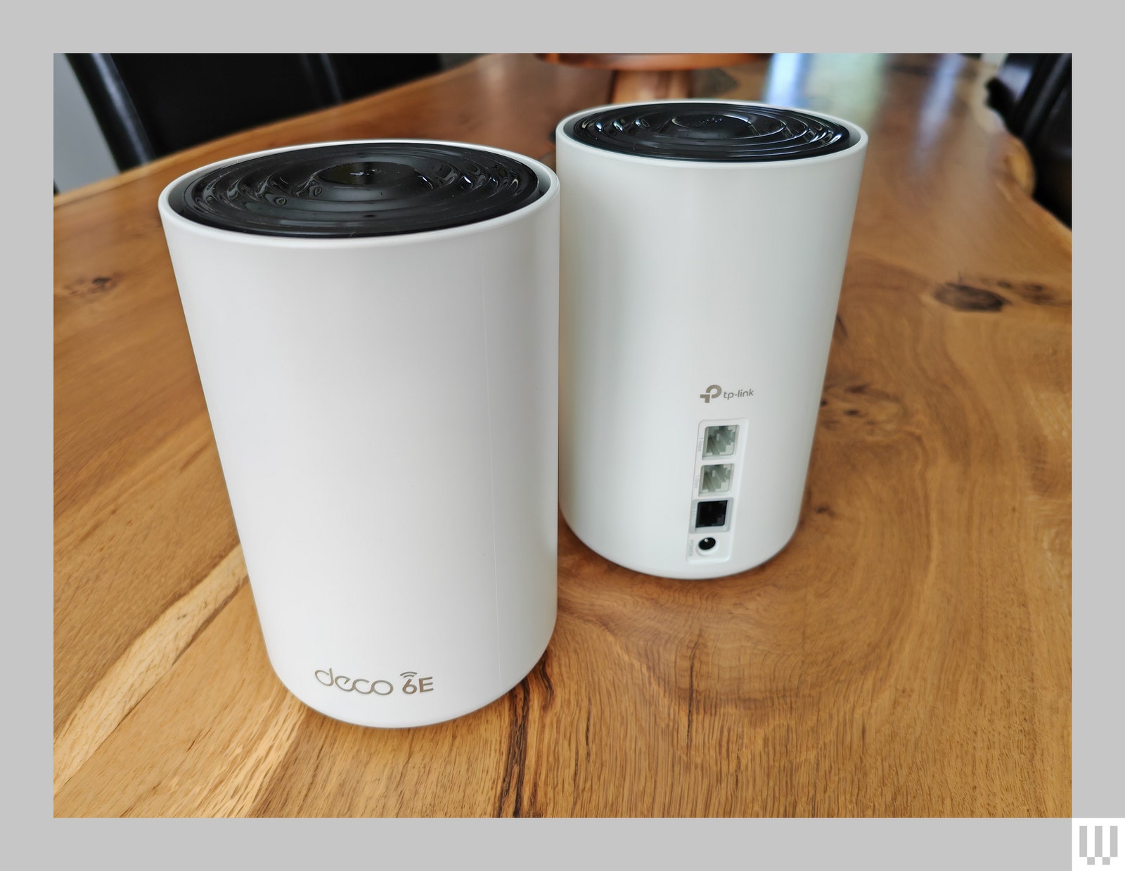 2 identical white cylindrical devices on a wooden table. One facing forward showing the logo and the other facing...