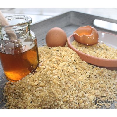 Quiko suplemento alimenticio con miel y huevo, se ven un tarro de miel, un huevo entero, una cáscara de huevo rota y el producto en forma de granulado amarillo.