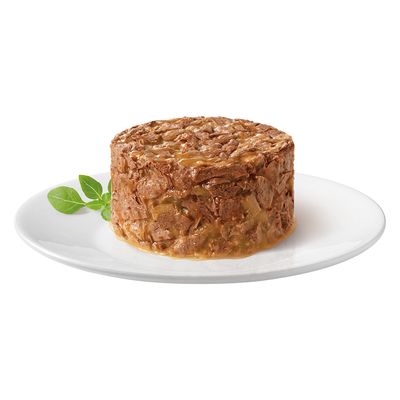 Porción de comida húmeda en forma redonda en plato blanco, decorada con hojas de albahaca.