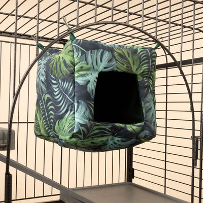 Cueva cúbica colgante con estampado de hojas tropicales, fijada a jaula metálica con clips. Adecuada como refugio para pequeños animales.
