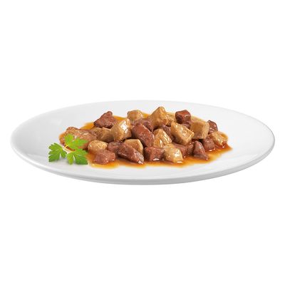 Primer plano de trozos de carne en salsa en un plato blanco, decorados con perejil.