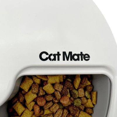 Cat Mate automatyczny podajnik karmy wypełniony suchą karmą, widoczna nazwa marki na białej obudowie.