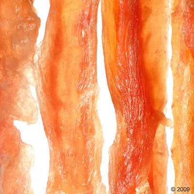 Narancsbarna színű, szárított húscsíkok közelről, valószínűleg háziállatoknak szánt snack vagy rágótermék. Narancsbarna színű, szárított húscsíkok közelről, valószínűleg háziállatoknak szánt snack vagy rágótermék.