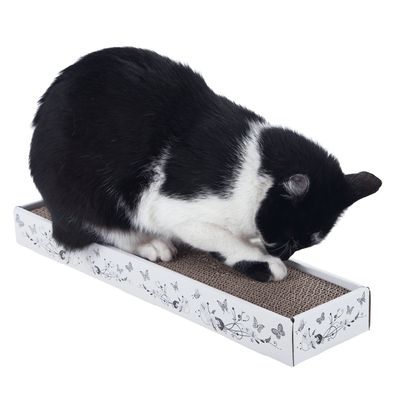 Black and white cat scratching on a rectangular cardboard scratching mat with decorative butterfly pattern.