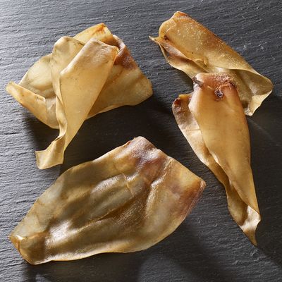 Négy szárított sertésfül sötét felületen, természetes rágóként látható.