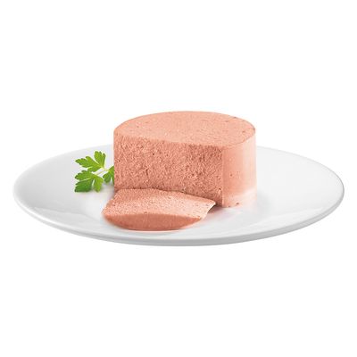 Rodaja de pastel de carne rosa en plato blanco, decorada con una hoja fresca de perejil.