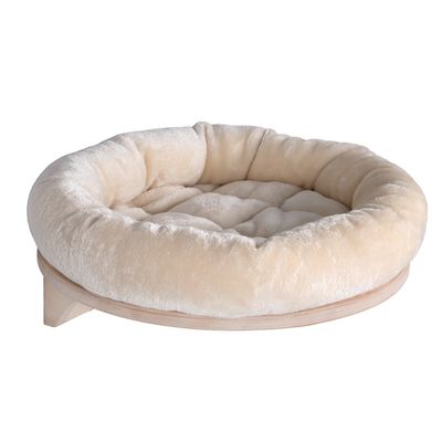 Wooden cat bed with beige padded edge, mounted on the wall. Grey cat sitting in the bed.
