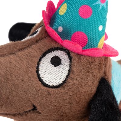 Juguete de peluche en forma de perro marrón con sombrero de fiesta, con puntos de colores y borde rosa.