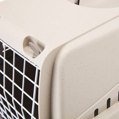 Primer plano de una caja de transporte beige con rejilla blanca y mecanismo de cierre gris.