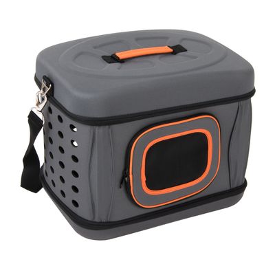Caja de transporte gris con asa naranja, orificios de ventilación laterales y ventana de malla. Correa de hombro desmontable y cremallera visible.